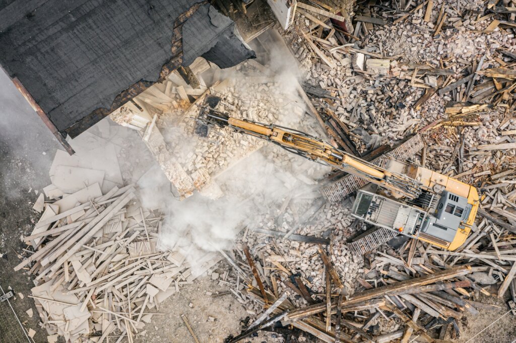 Yellow excavator destroys building. Heavy duty machine is demolishing a brick building. Demolition of the building . Demolition construction work aerial drone photo